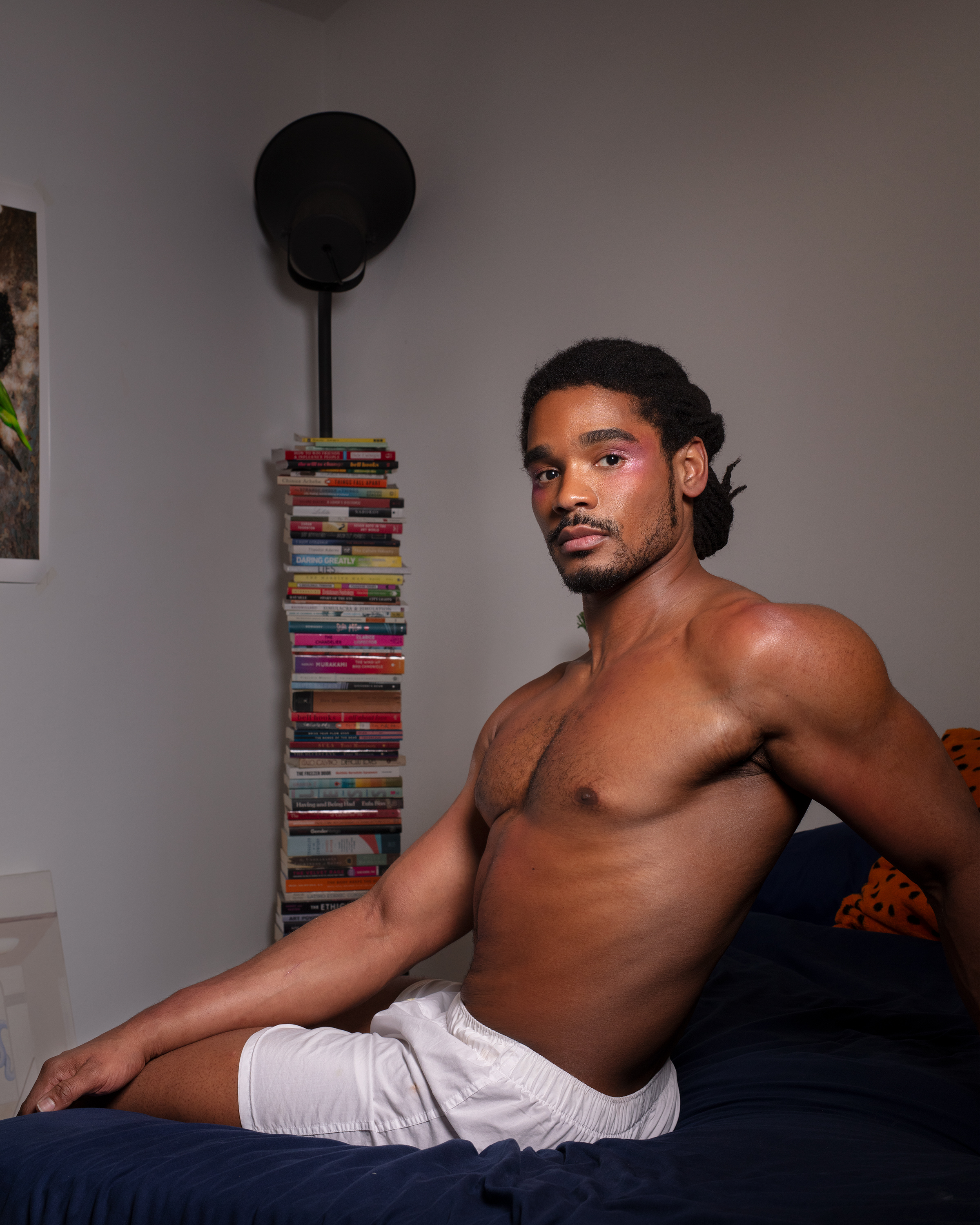 Khalyle leaning with one arm back on a bed in white shorts twisting to look at the camera